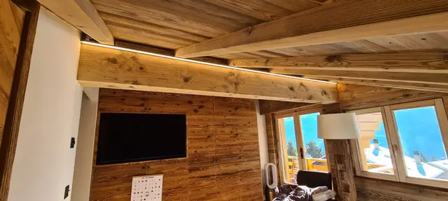 Éclairage LED indirect sur poutre dans un séjour de chalet avec vue sur le lac